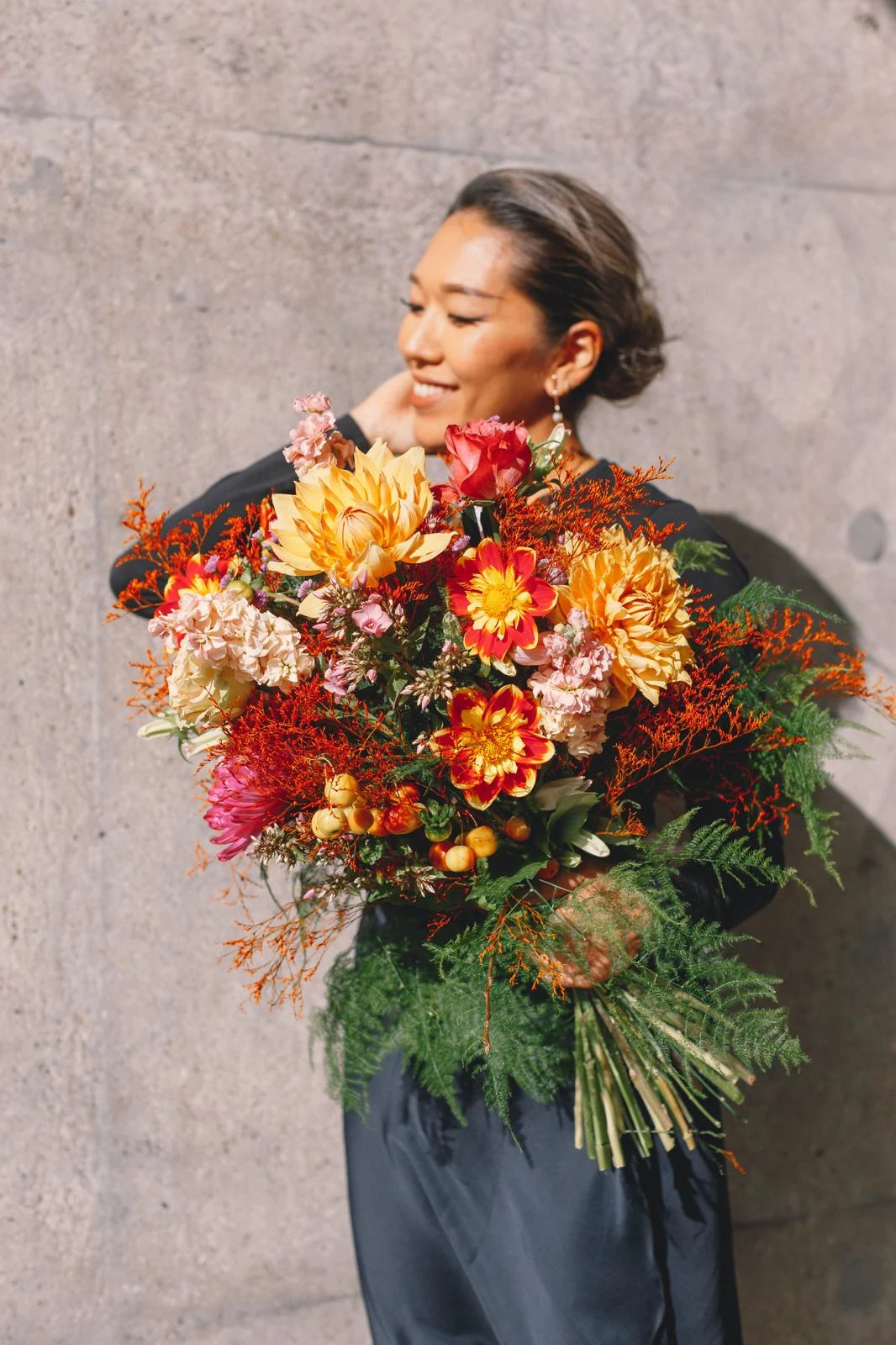Woman holding an oversized bouquet against a stone wall